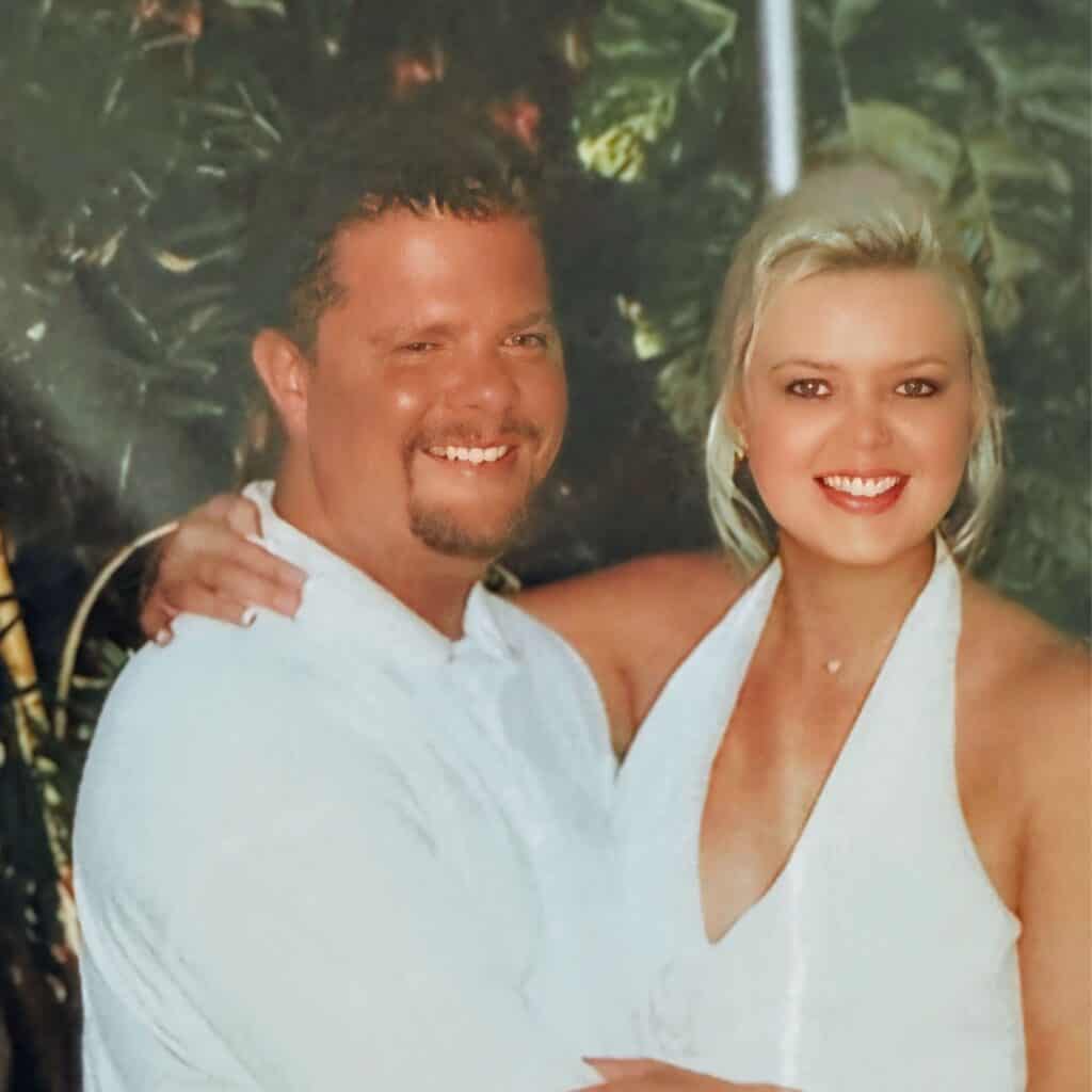 Kristy and Scott smiling on their wedding day in white outfits, celebrating love and joy