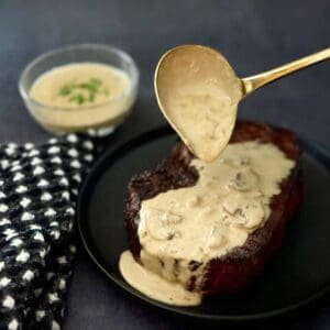 Rich creamy mushroom steak sauce poured over seared steak with a golden spoon