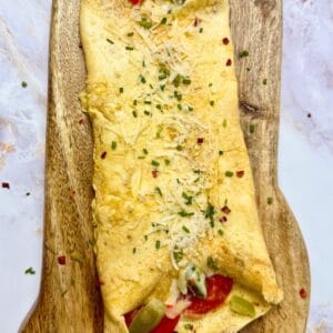 Easy keto pizza omelet folded and topped with Parmesan, herbs, and red pepper flakes on a wooden board.
