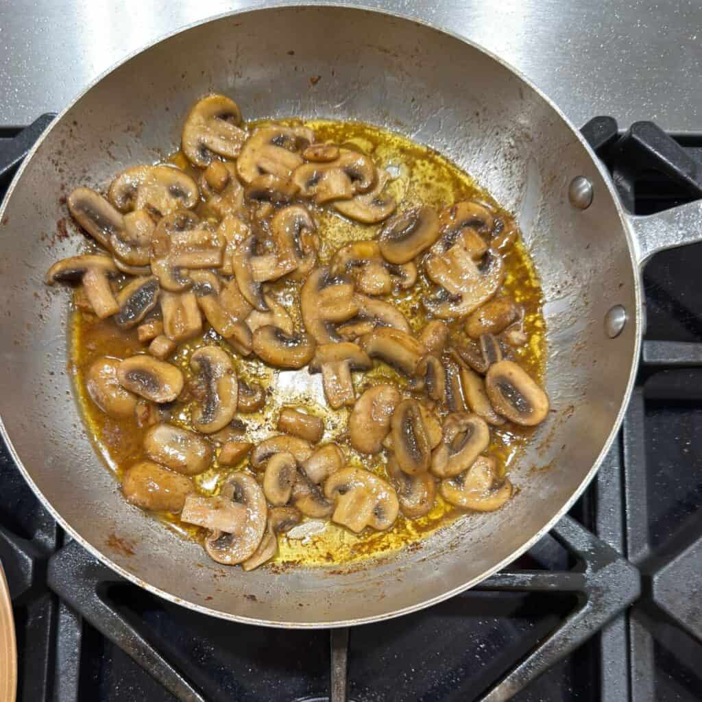 Sliced mushrooms sautéing in butter and olive oil in a stainless steel skillet on the stovetop — the first step in building a rich creamy mushroom steak sauce.