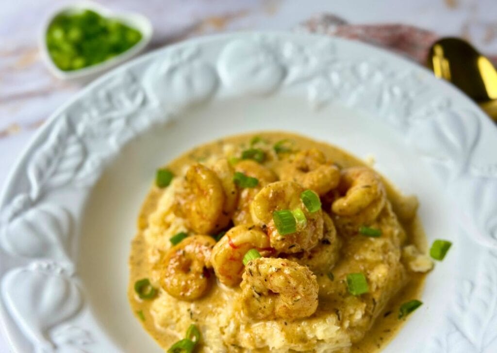 Keto Cajun shrimp and cheesy cauliflower grits topped with sliced green onions on a white plate.