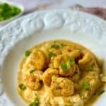 Easy Keto Cajun shrimp and cheesy cauliflower grits topped with sliced green onions on a white plate.