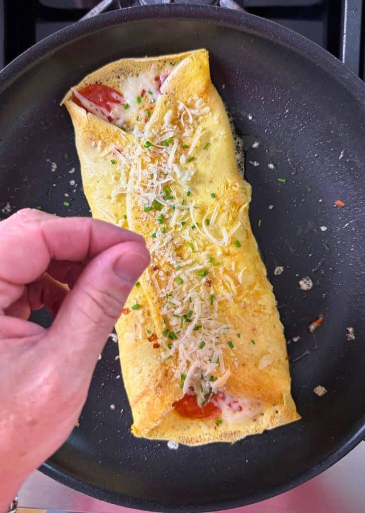 Easy keto pizza omelet fully cooked pizza omelet in a skillet, topped with shredded cheese, herbs, and pepperoni, just before serving.