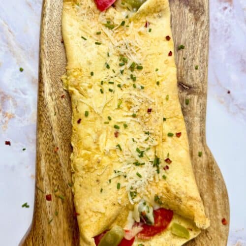 Scott’s Pizza Omelet filled with peppers and melted cheese, folded and topped with herbs on a wooden board