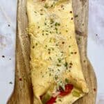 Easy Keto Pizza Omelet on a wooden board, folded and topped with melted cheese, herbs, and red pepper flakes.